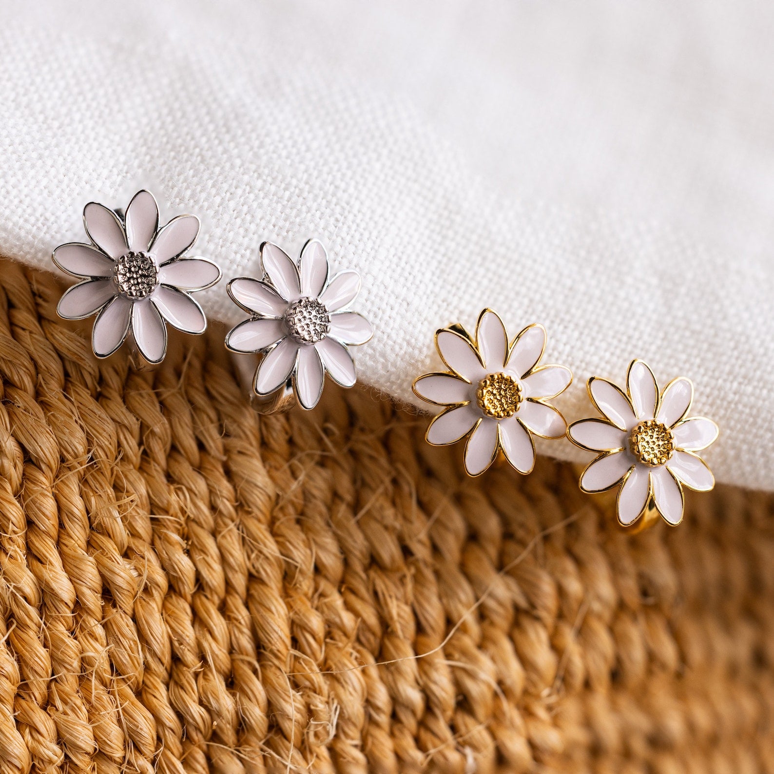 Two pairs of Daisy Huggies—one in silver and one in gold—are displayed on fabric and woven material, offering minimalist flower earrings ideal for jewelry lovers.