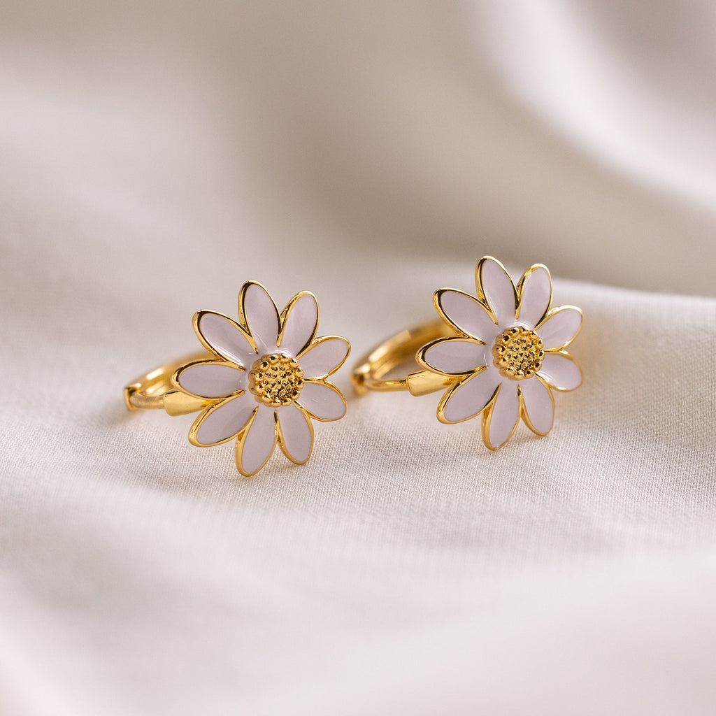 Daisy Huggies: minimalist gold rings featuring white daisy flower designs, ideal for subtle elegance, displayed on a soft, cream fabric backdrop.