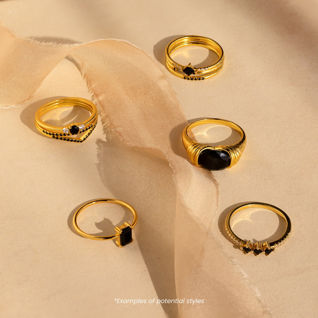 Five Mystery Rings featuring black and white stones, from an eclectic jewelry collection, are displayed on beige fabric in soft sunlight.