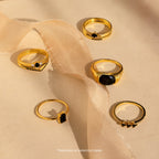 Five Mystery Rings featuring black and white stones, from an eclectic jewelry collection, are displayed on beige fabric in soft sunlight.