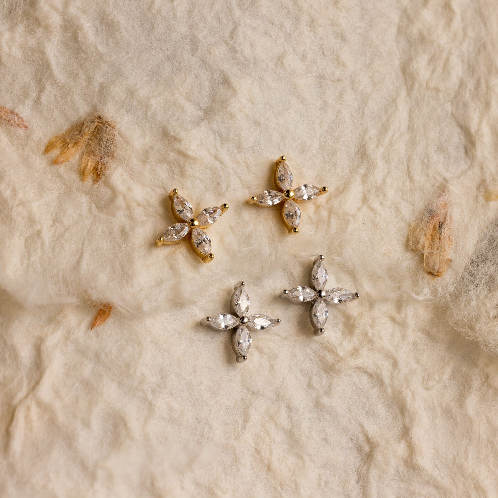 The Marquise Diamond Flower Studs, available in gold and silver, are displayed on textured fabric—ideal as wedding jewelry or for adding floral elegance to any outfit.