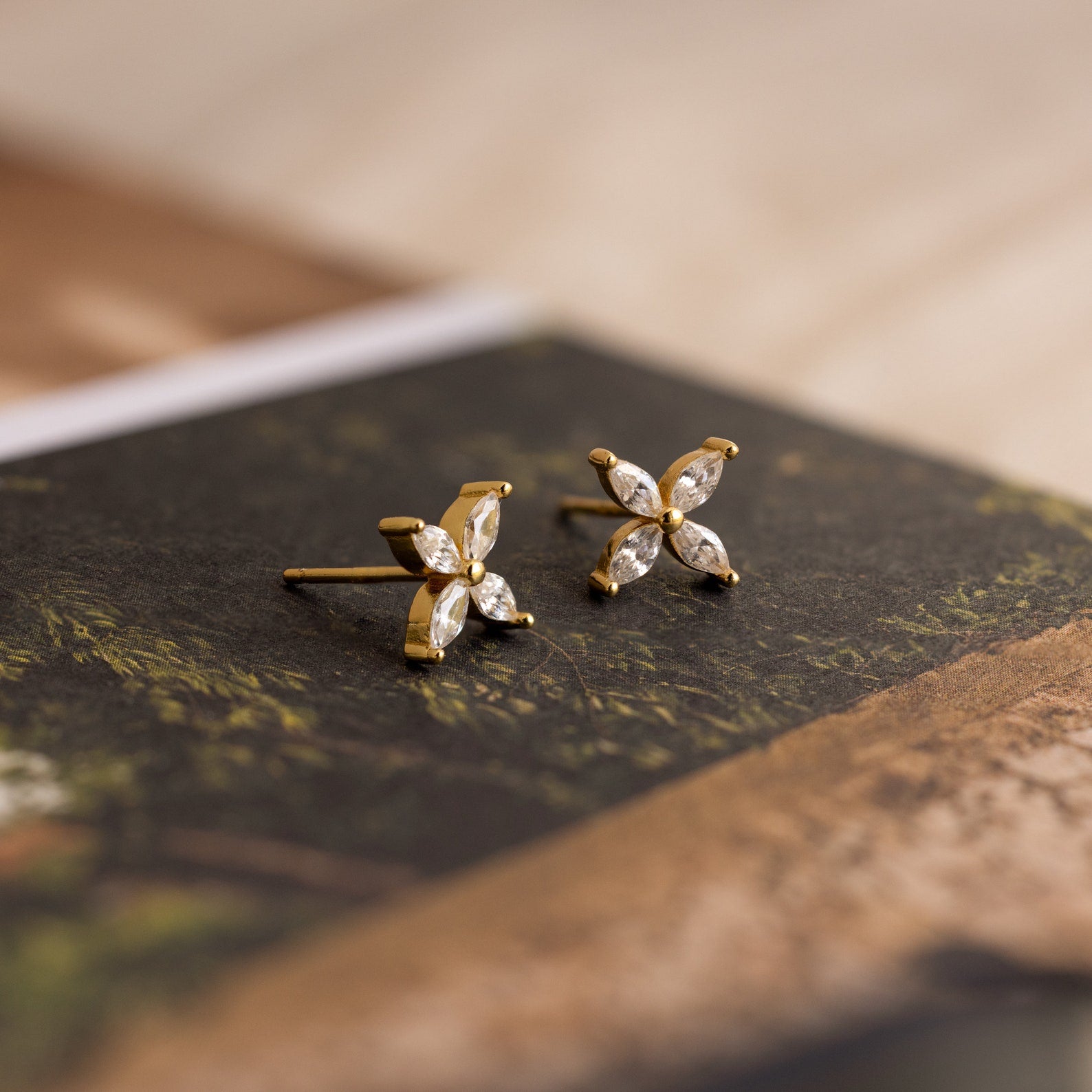 Marquise Diamond Flower Studs with four leaf-shaped clear stones in a floral design, elegantly displayed on a book—perfect as floral earrings and exquisite wedding jewelry.