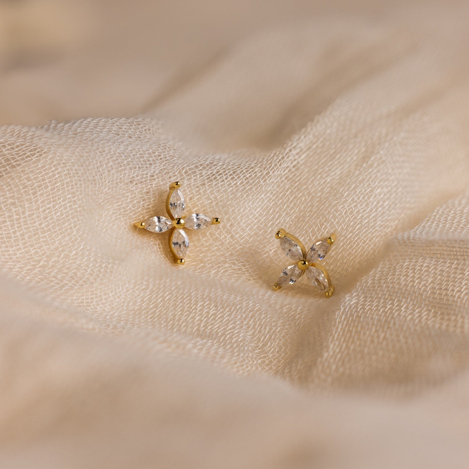 Marquise Diamond Flower Studs featuring gold and crystal details rest elegantly on cream-colored fabric—ideal floral earrings for weddings or special occasions.