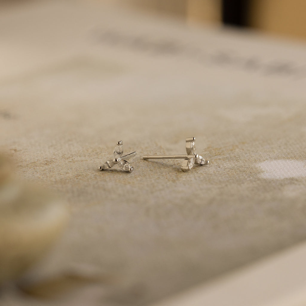 Close-up of the Trio Floral Marquise Studs, featuring delicate silver and small gemstones on a textured neutral surface—an elegant earring set inspired by classic diamond designs.