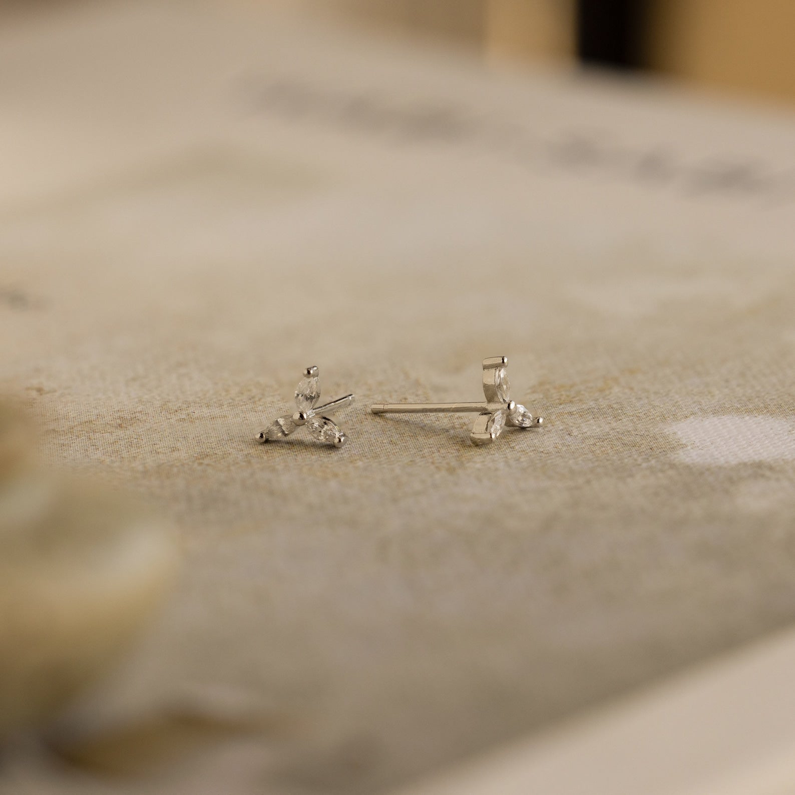 Close-up of the Trio Floral Marquise Studs, featuring delicate silver and small gemstones on a textured neutral surface—an elegant earring set inspired by classic diamond designs.