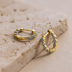 Inside Out Ivy Huggies featuring light blue gemstones are displayed on a textured beige stone surface.