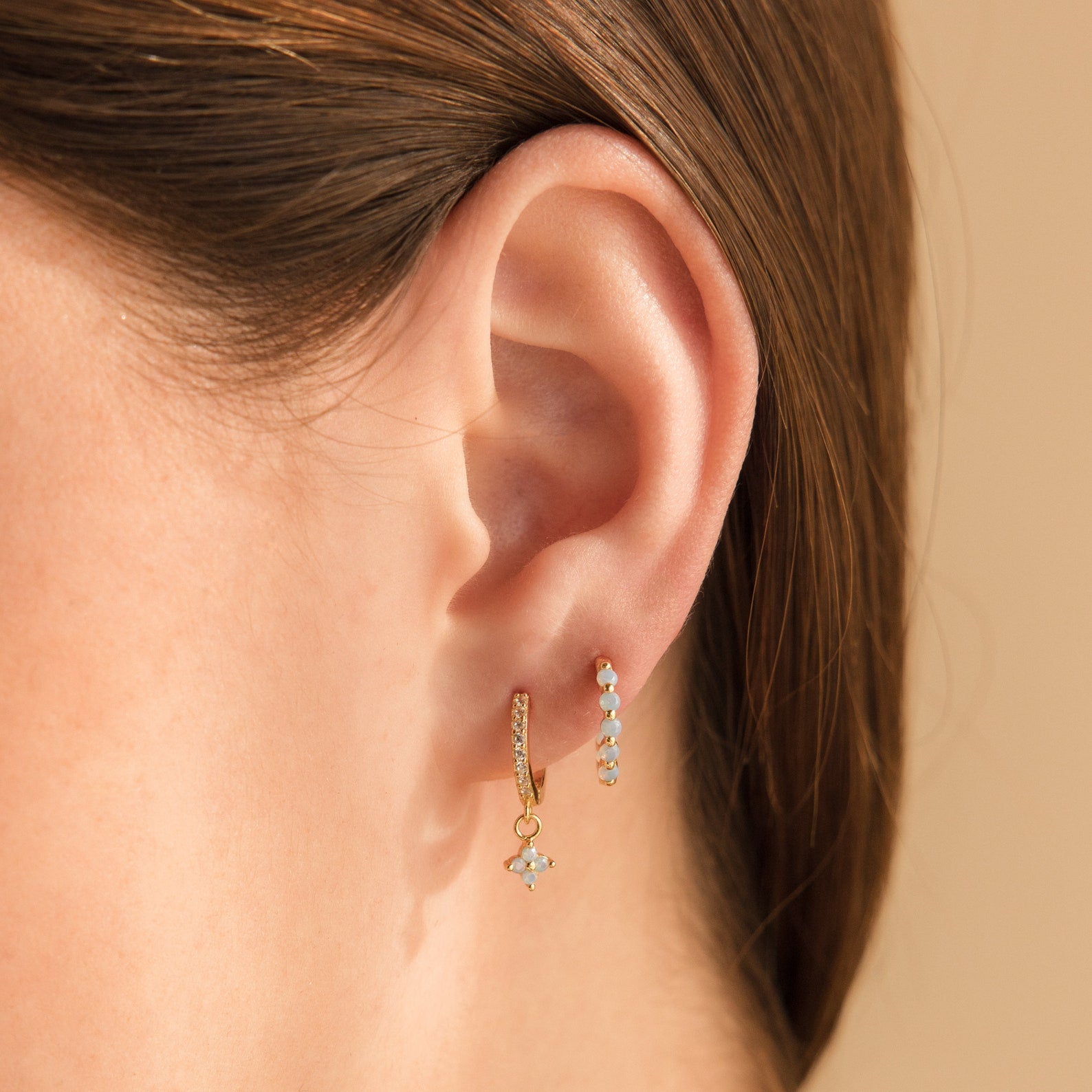 Close-up of a woman's ear wearing Inside Out Ivy Huggies—gold hoops adorned with light blue gemstones and delicate dangling charms.