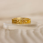The Filigree Flower Ring features a gold band with intricate scrollwork and small embedded diamonds, evoking vintage charm and displayed elegantly on a clear, curved stand.