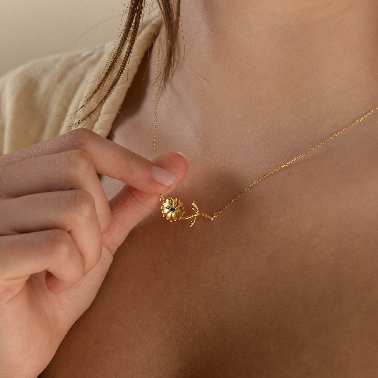 A person holds a Flower Birthstone Necklace near their chest, wearing a light beige top—a stunning custom piece that adds personalized charm to any outfit.