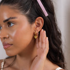 A woman with long dark hair wears the Puff Heart Charm Huggies and holds her hand to her ear.