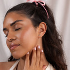 Woman with closed eyes touching her neck, wearing a pink ribbon in her hair and elegant Trio Cluster Pearl Studs earrings.