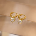 Diamond Heart Drop Huggies—coquette-inspired gold hoop earrings with sparkling diamond heart charms—displayed on a soft beige surface.
