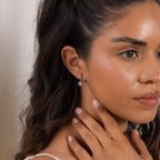 A coquette-inspired woman with wavy dark hair wears Diamond Heart Drop Huggies and gently touches her neck, gazing to the side.