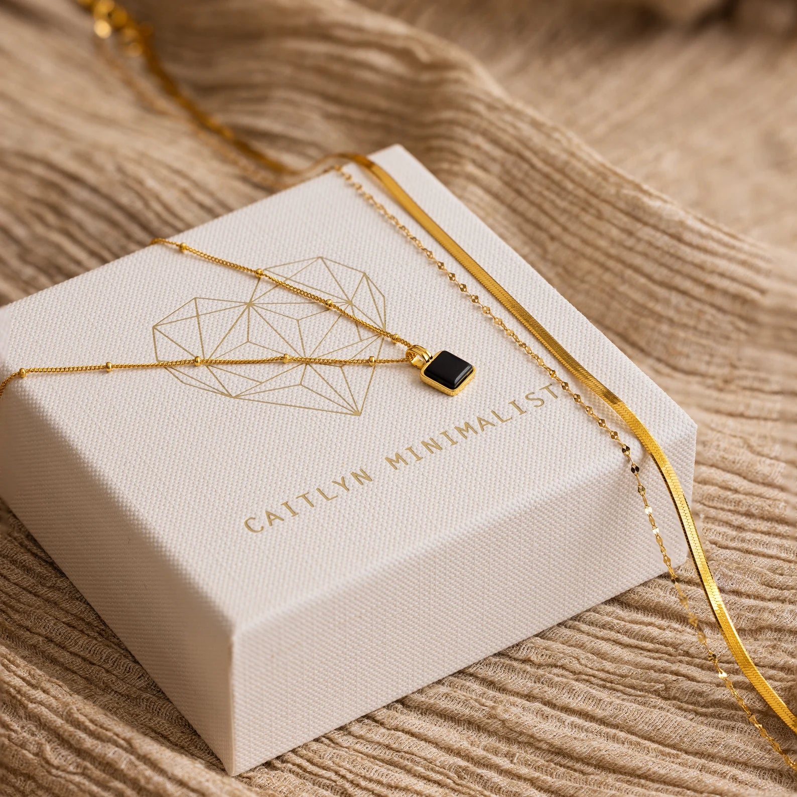 Mystery Necklace Box: Gold necklaces elegantly displayed on textured fabric with a Caitlyn Minimalist jewelry box—ideal for your collection or as a surprise gift.
