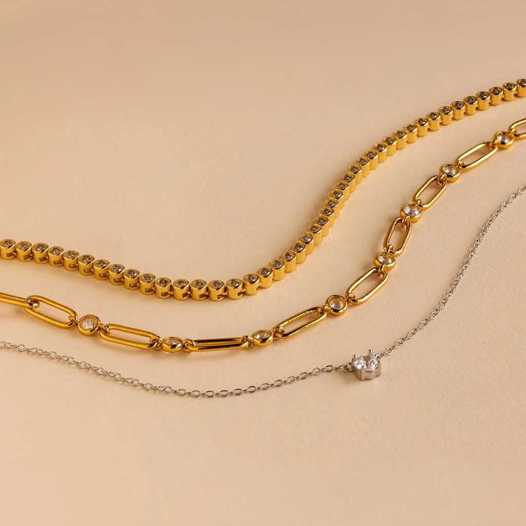 Three necklaces from the Mystery Necklace Box on a beige background: two gold chains and one delicate silver chain with a small pendant—ideal for your jewelry collection or as a special surprise.