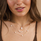 Close-up of a woman in a brown top wearing layered pearl, gold, and silver necklaces—a chic style that can be discovered in the Mystery Necklace Box.