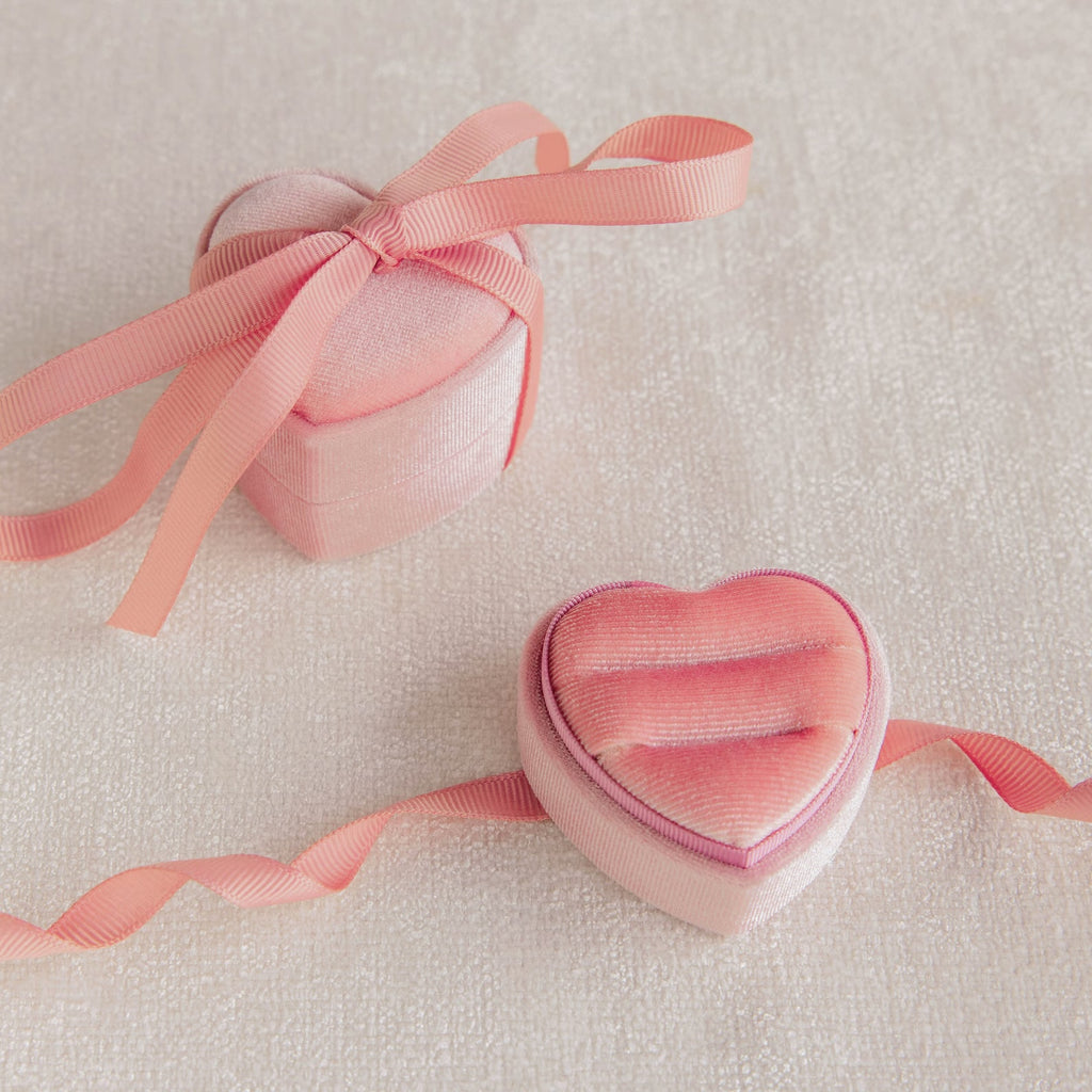 Two Pink Velvet Heart Ring Boxes, one open and one closed, adorned with ribbons, rest elegantly on a light textured surface—perfect as a charming display or jewelry case.