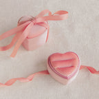 Two Pink Velvet Heart Ring Boxes, one open and one closed, adorned with ribbons, rest elegantly on a light textured surface—perfect as a charming display or jewelry case.