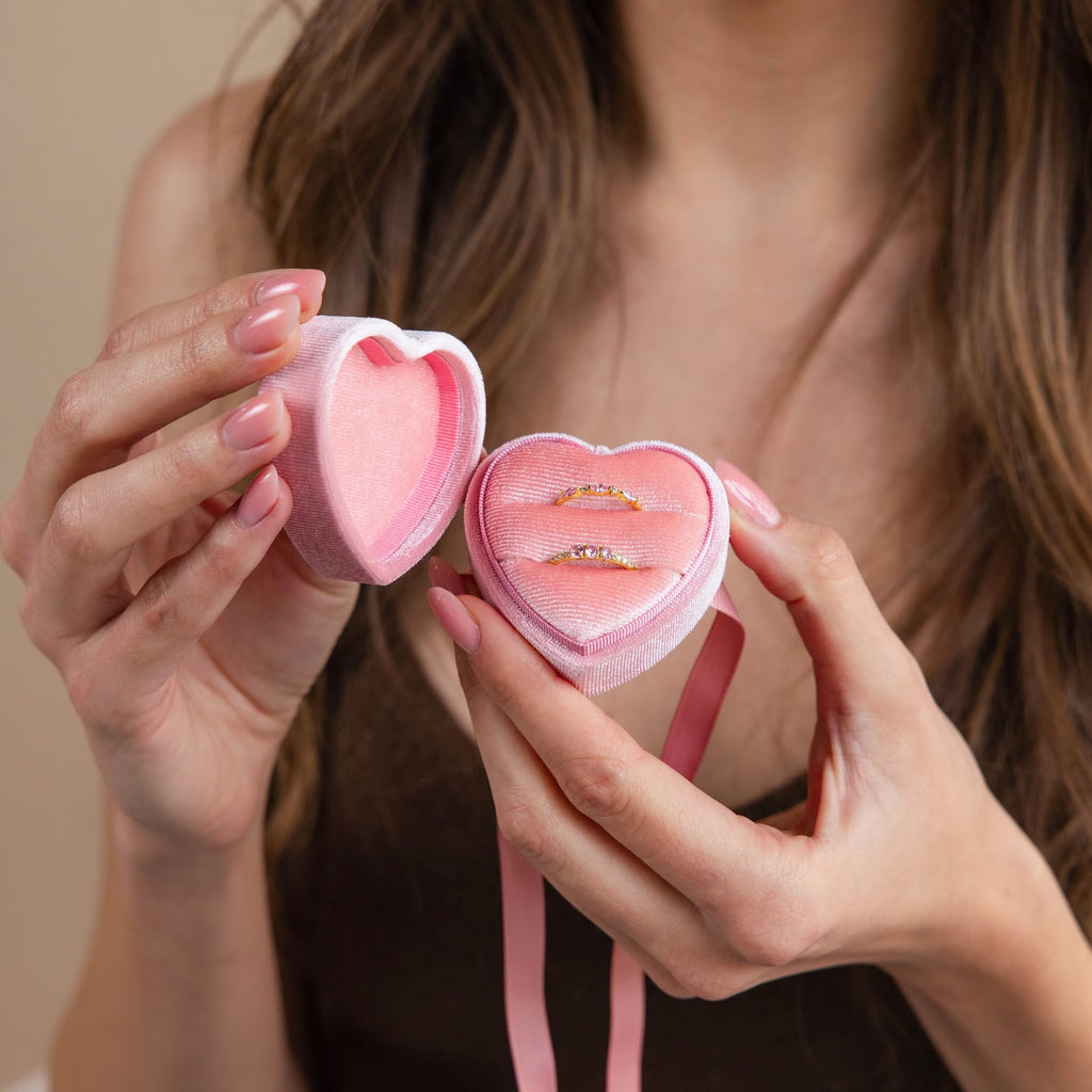 A woman holds an open Pink Velvet Heart Ring Box, displaying two gold rings inside.