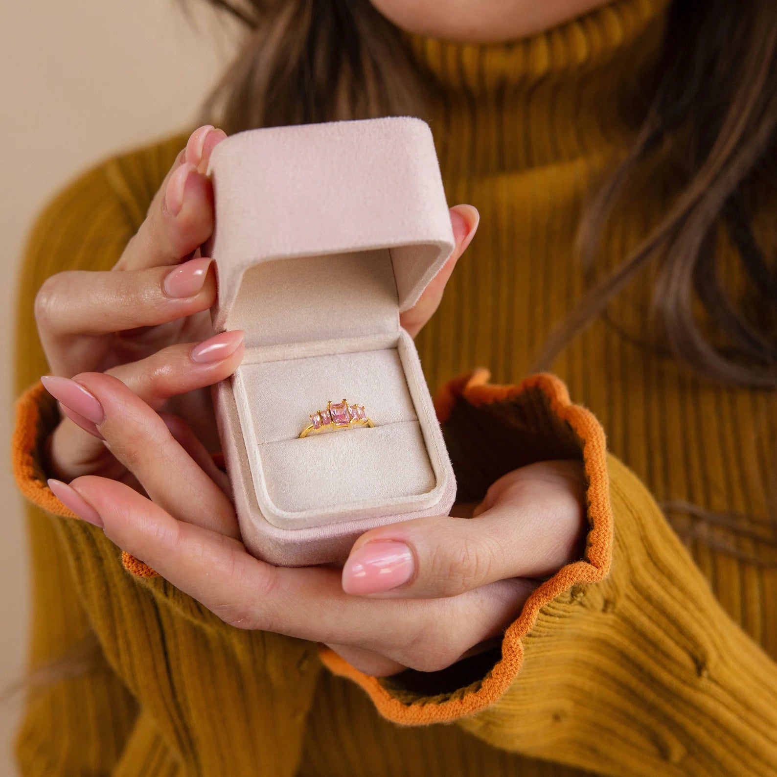 Woman in mustard sweater holds a Pink Suede Ring Box containing a gemstone ring, highlighting its chic minimalist design.