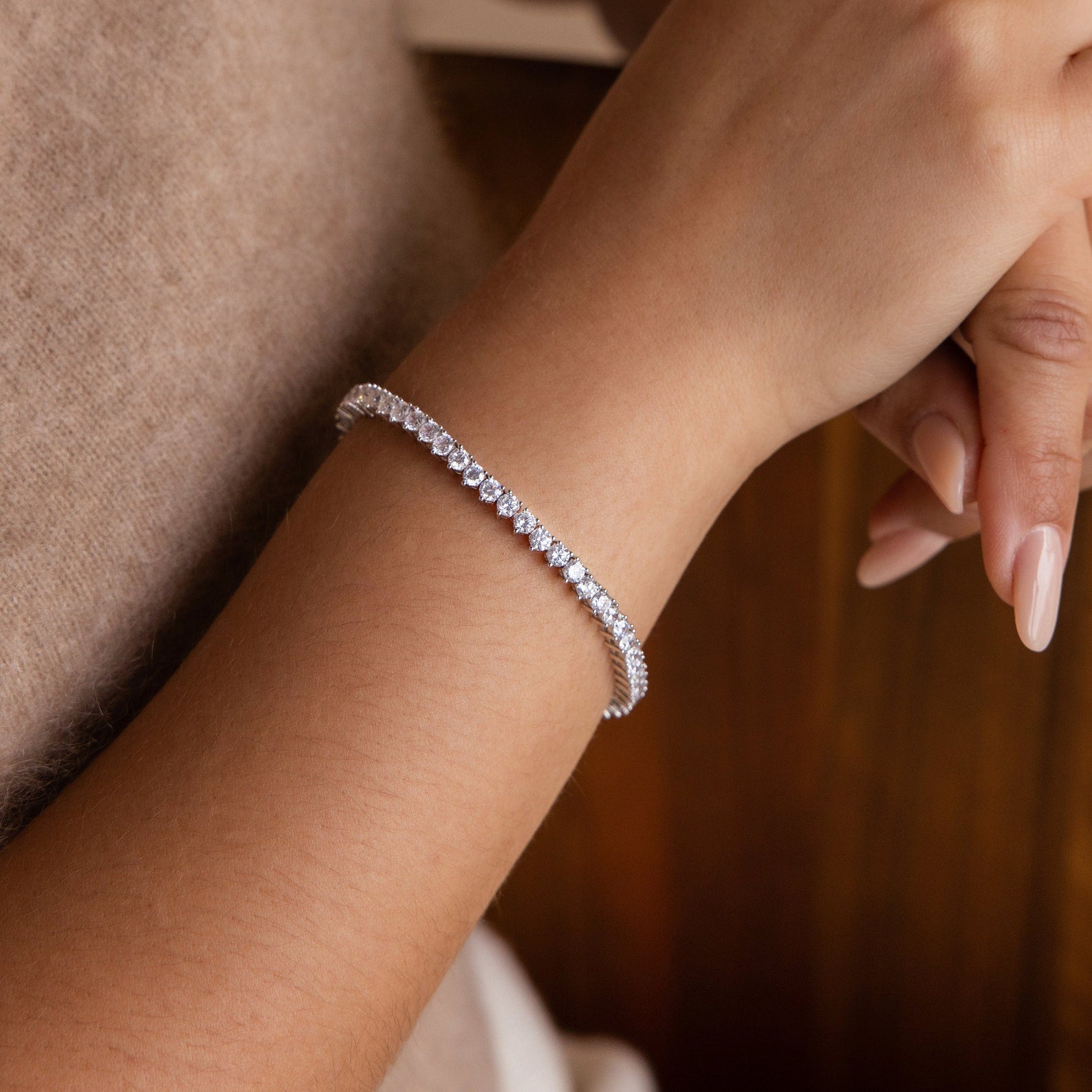 A woman's hand with nude manicured nails wears the 3-Prong Diamond Tennis Necklace & Bracelet Set in White Gold, showcasing its delicate sparkle and elegant design.