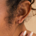 Close-up of an ear adorned with the Dainty Pave Birthstone Huggies—a delicate gold hoop earring—while a manicured hand gently touches the neck.