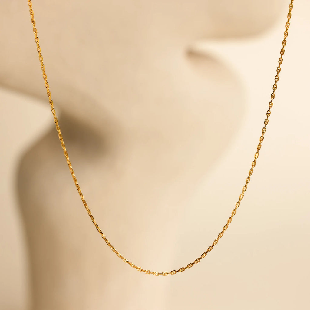 The Skinny Mariner Chain Necklace is shown on a soft, blurred beige background with minimal curves—an elegant, minimalist piece perfect for everyday wear and layering.