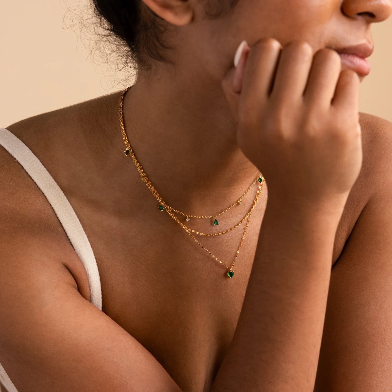A woman showcases an effortlessly chic everyday look, resting her chin on her hand while wearing the Skinny Mariner Chain Necklace layered with green gemstone pendants.