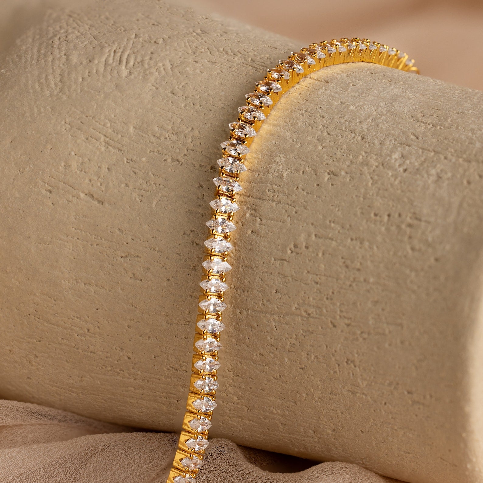 Detailed view of the Marquise Diamond Tennis Bracelet draped over a neutral textured surface, showcasing the brilliance of the marquise-cut stones.