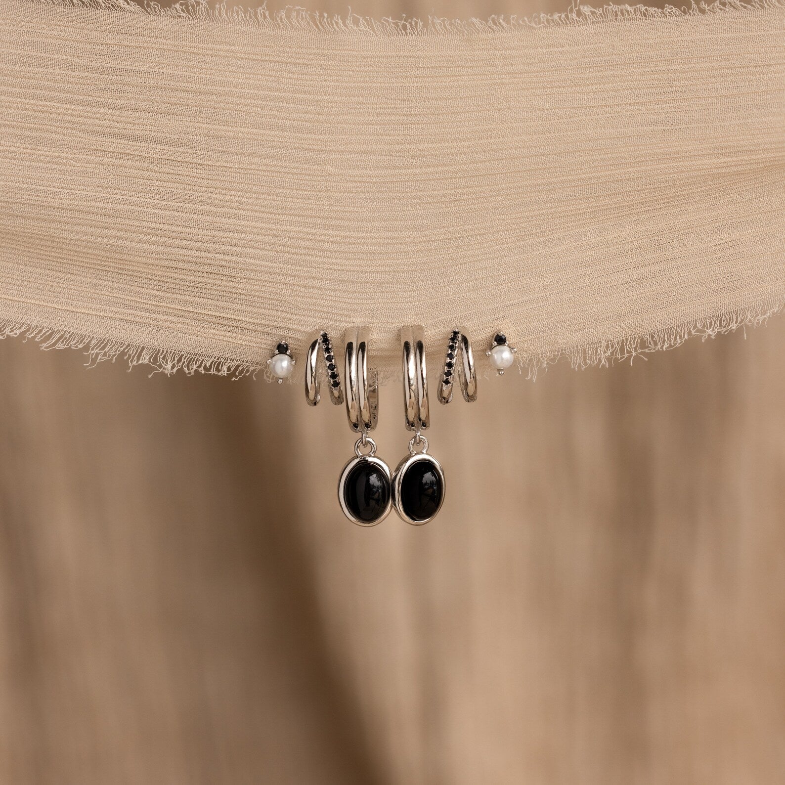 Five sterling silver earrings from the Mystery Earrings Box, featuring black and white accents, are displayed on textured beige fabric—an ideal gift in a stylish Velvet Earring Box.