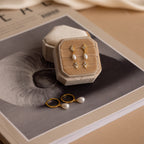 The Mystery Earrings Box in 18K Gold from our jewelry collection, displayed in a beige box, is set on a magazine featuring a shell image.