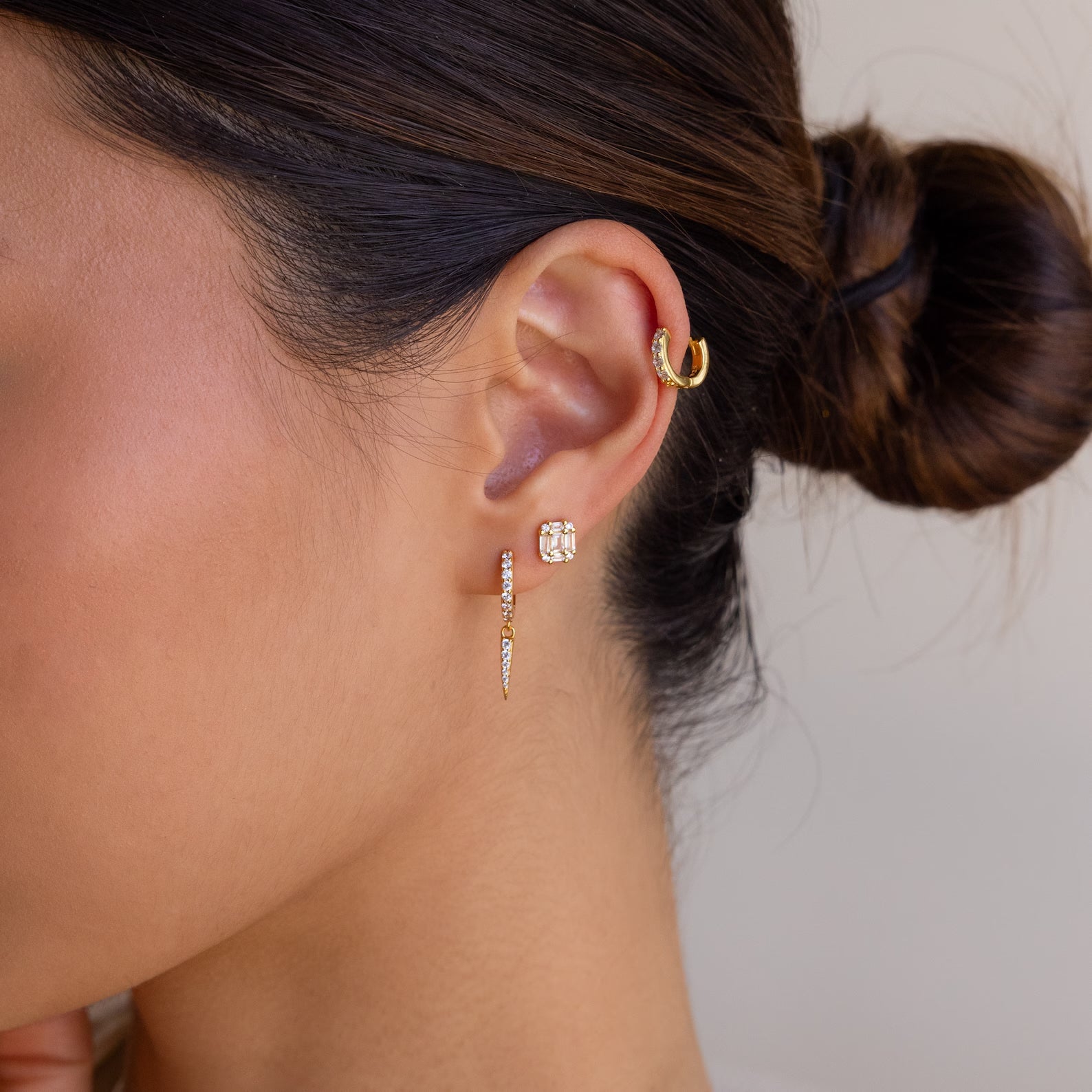 Close-up of a woman's ear with four gold earrings, her dark hair in a bun—perfect inspiration for your own Mystery Earrings Box collection.