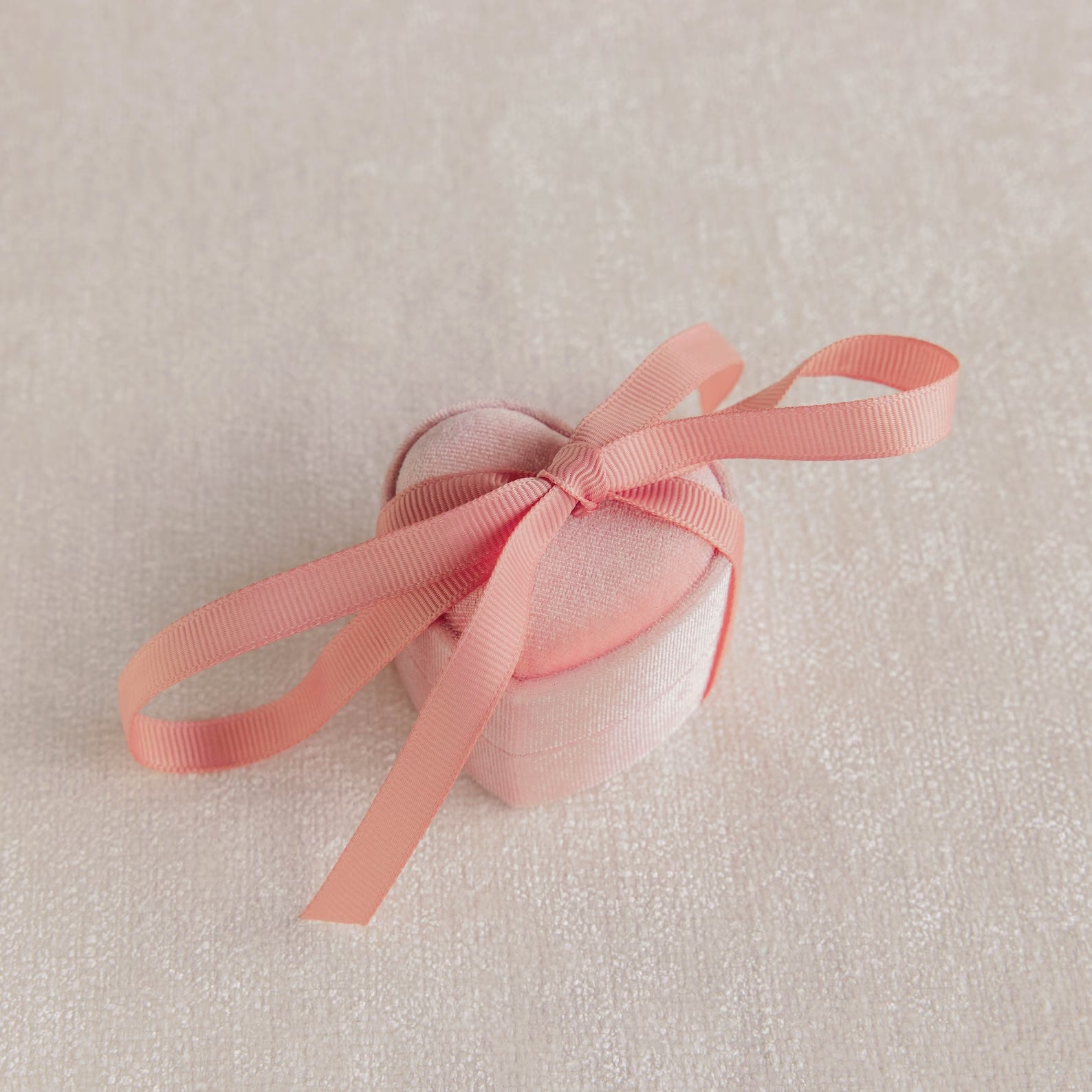 The Pink Velvet Heart Ring Box features a small, heart-shaped coquette design in pink with a matching ribbon bow—ideal as a jewelry case and displayed on a light textured surface.