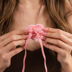 A woman holds a pink heart-shaped ornament with bow and ribbon close to her chest, exuding coquette style—perfect for showcasing or gifting the Pink Velvet Heart Ring Box.