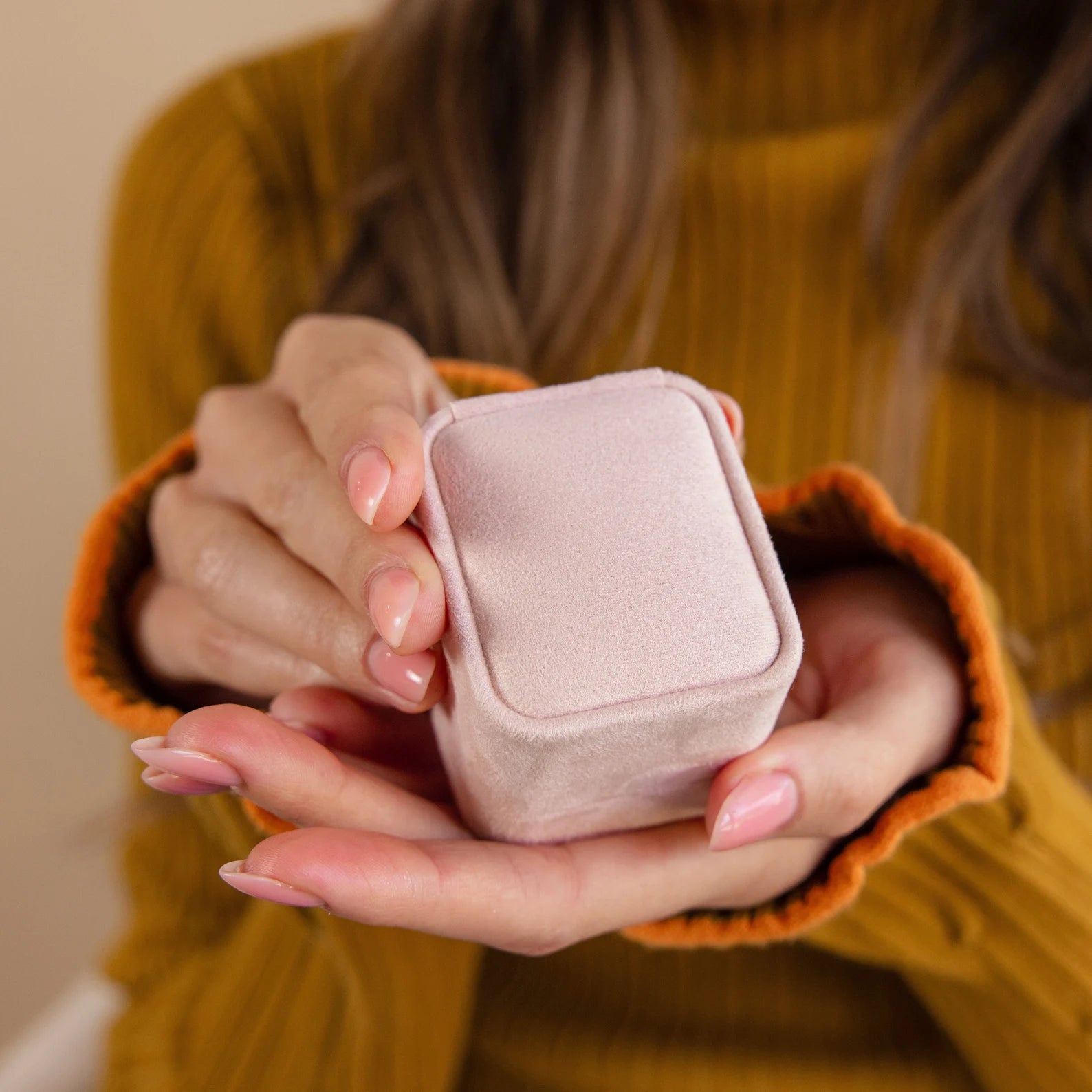 A woman in a mustard sweater holds the Pink Suede Ring Box, featuring a closed, minimalist design in light pink suede.