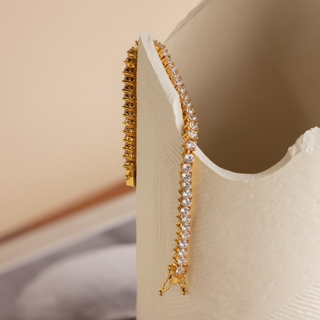 The 3 Prong Tennis Bracelet drapes elegantly over a cream-colored textured ceramic vase, showcasing its timeless beauty and sophistication.