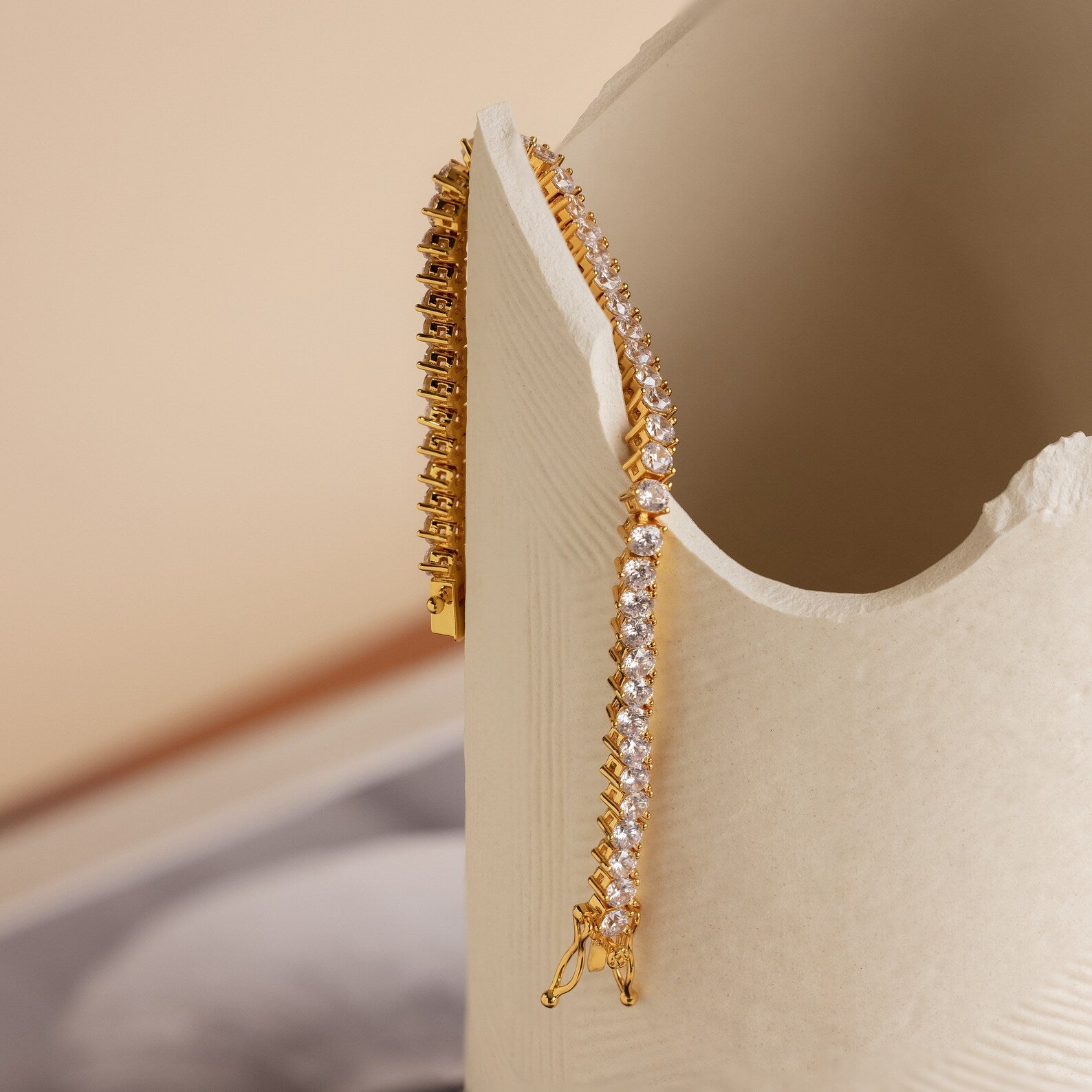 The 3 Prong Tennis Bracelet drapes elegantly over a cream-colored textured ceramic vase, showcasing its timeless beauty and sophistication.