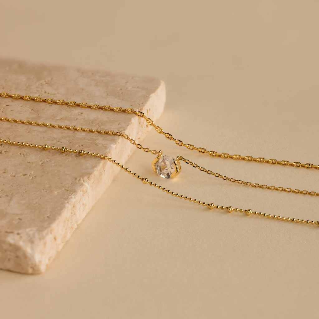 The Skinny Mariner Chain Necklace, elegantly displayed on a beige stone surface, is perfect for everyday wear or layering to achieve a chic look.
