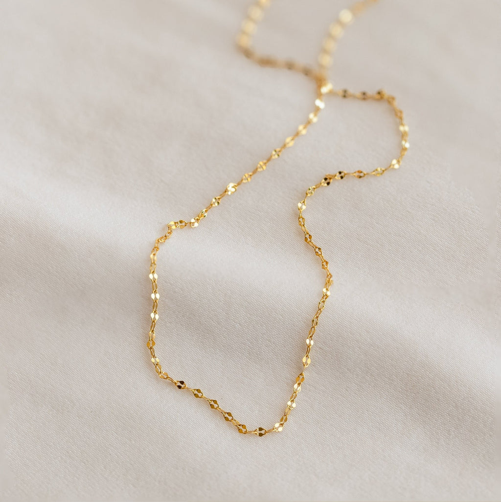 The Dainty Diamond Necklace Set, featuring delicate gold links, is displayed on a soft, light-colored fabric background.