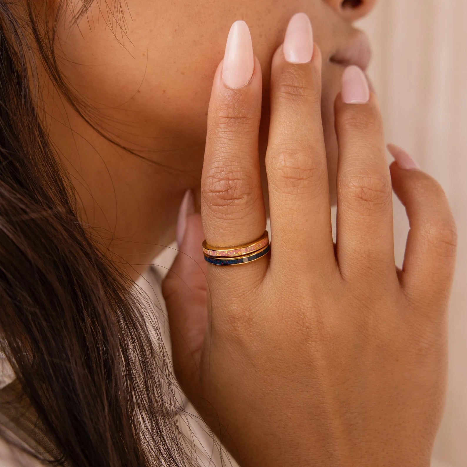 A person with manicured nails wears three stacked gold rings from the Opal Inlay Rings Set, featuring striking opal details and indigo blue accents.
