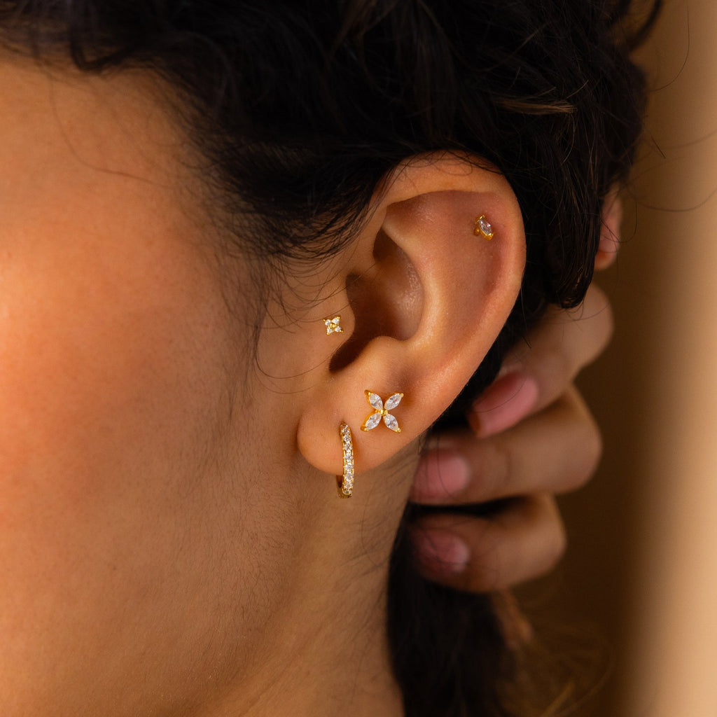 A close-up of an ear adorned with gold and diamond Birthstone Flower Studs and a small hoop, highlighting the elegance of personalized earrings.