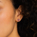 Close-up of a woman's ear wearing the Birthstone Flower Studs—small, purple, flower-shaped gemstone earrings—perfect personalized jewelry for any occasion.