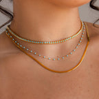 Close-up of a woman's neck adorned with the Turquoise Bezel Tennis Necklace, layered with gold necklaces and a delicate choker for a chic, elegant look.