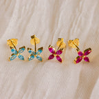Two pairs of Birthstone Flower Studs, featuring blue and pink marquise-cut stones in gold, rest on cream fabric—ideal for adding color to your collection or wearing as personalized earrings.