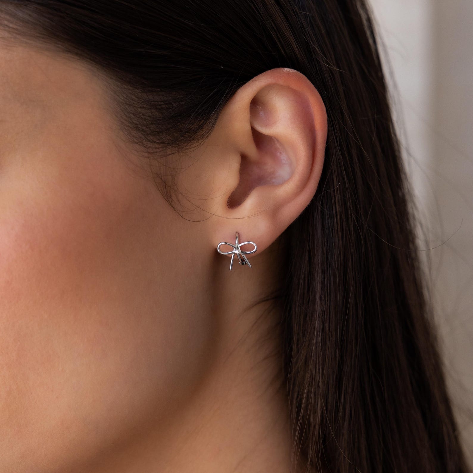 A close-up of a woman's ear adorned with Classic Ribbon Bow Huggies—dainty silver bow-shaped earrings that add the perfect feminine touch.