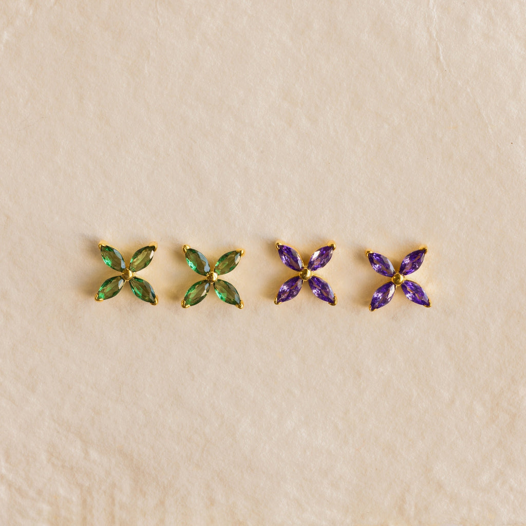 Two pairs of Birthstone Flower Studs—one with green and one with purple gemstones—are showcased on a beige background, making them perfect personalized earrings for any occasion.