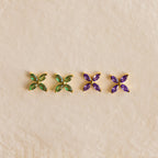 Two pairs of Birthstone Flower Studs—one with green and one with purple gemstones—are showcased on a beige background, making them perfect personalized earrings for any occasion.