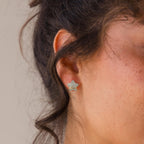 Close-up of a woman's ear wearing Aquamarine Moon & Star Studs, featuring dainty silver accents and wavy brown hair.