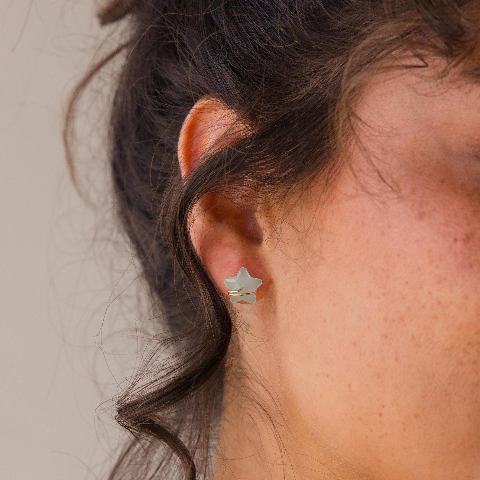 Close-up of a woman's ear wearing Aquamarine Moon & Star Studs, featuring dainty silver accents and wavy brown hair.