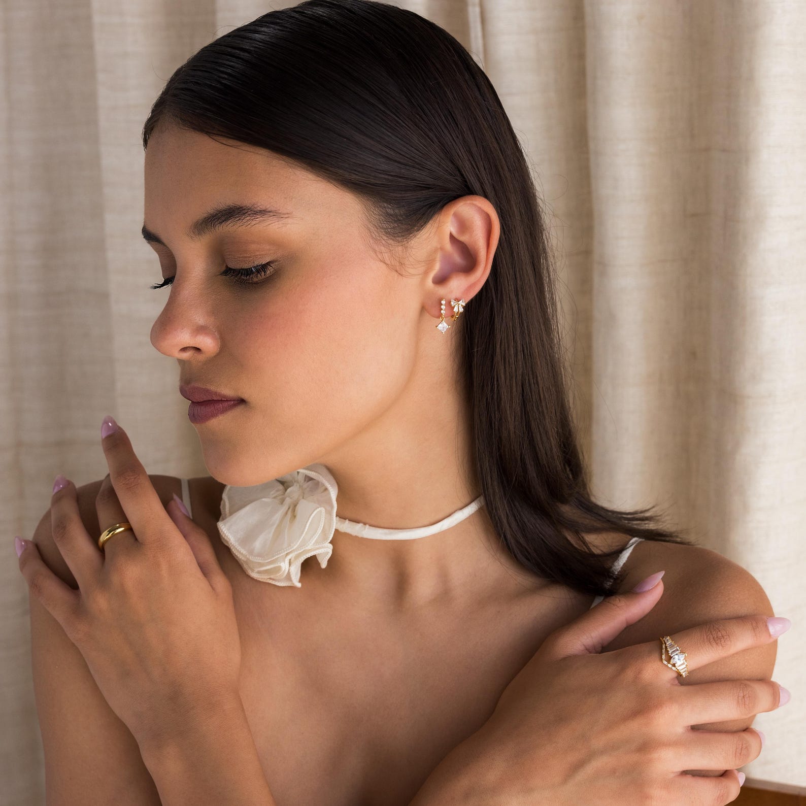 Model showcases Diamond Ribbon Bow Huggies paired with Diamond Drop Earrings, a Gold Dome Ring, and a Curved Diamond Ring. 